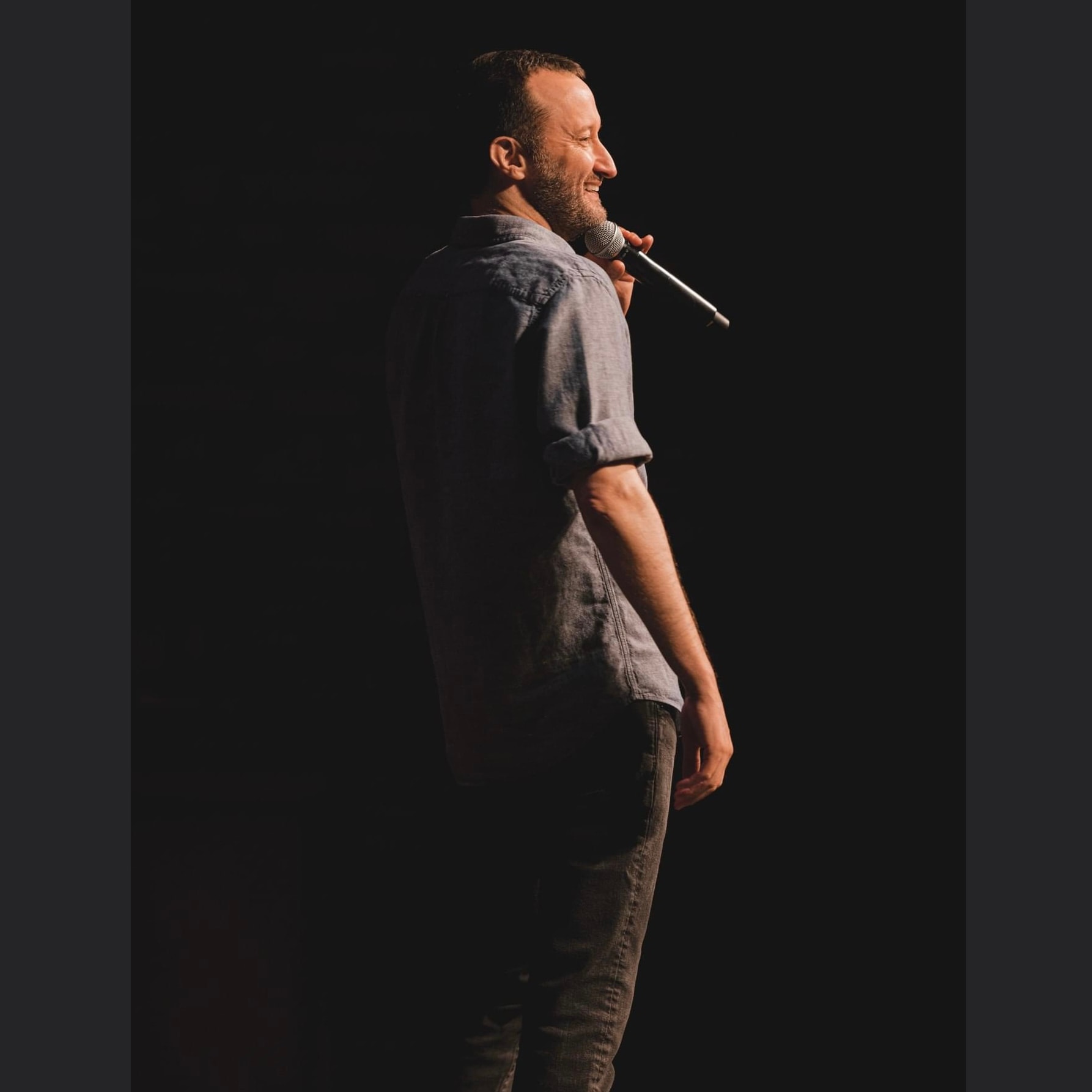 Dan Mengini performing on stage, profile view with mic